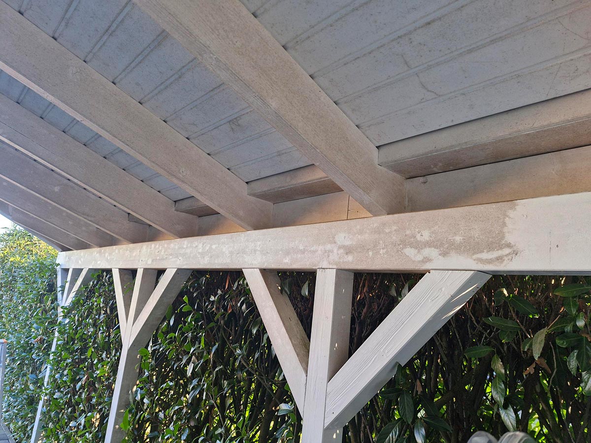Ein hölzernes Carport-Dach in hellem Grau mit verwitterten Stellen und Schatten