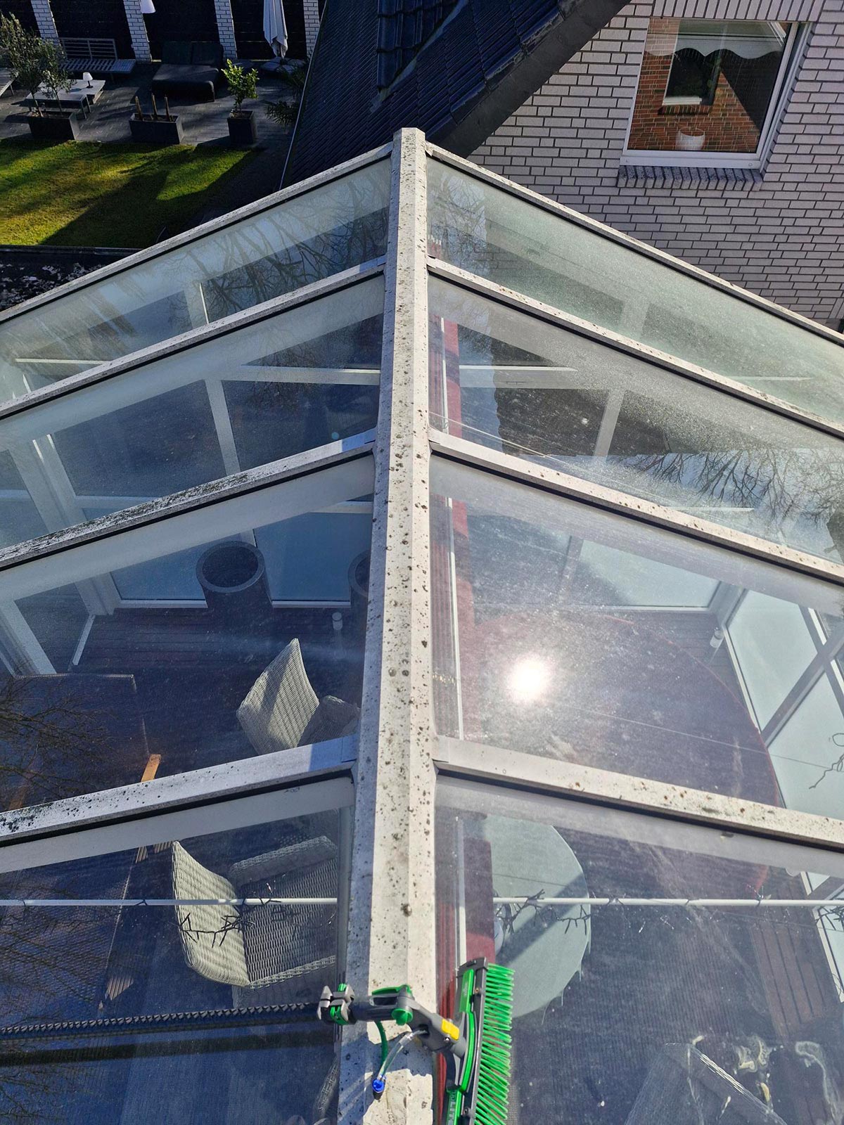 Glasüberdachung mit grüner Bürste in der Sonne und Blick auf Gartenmöbel