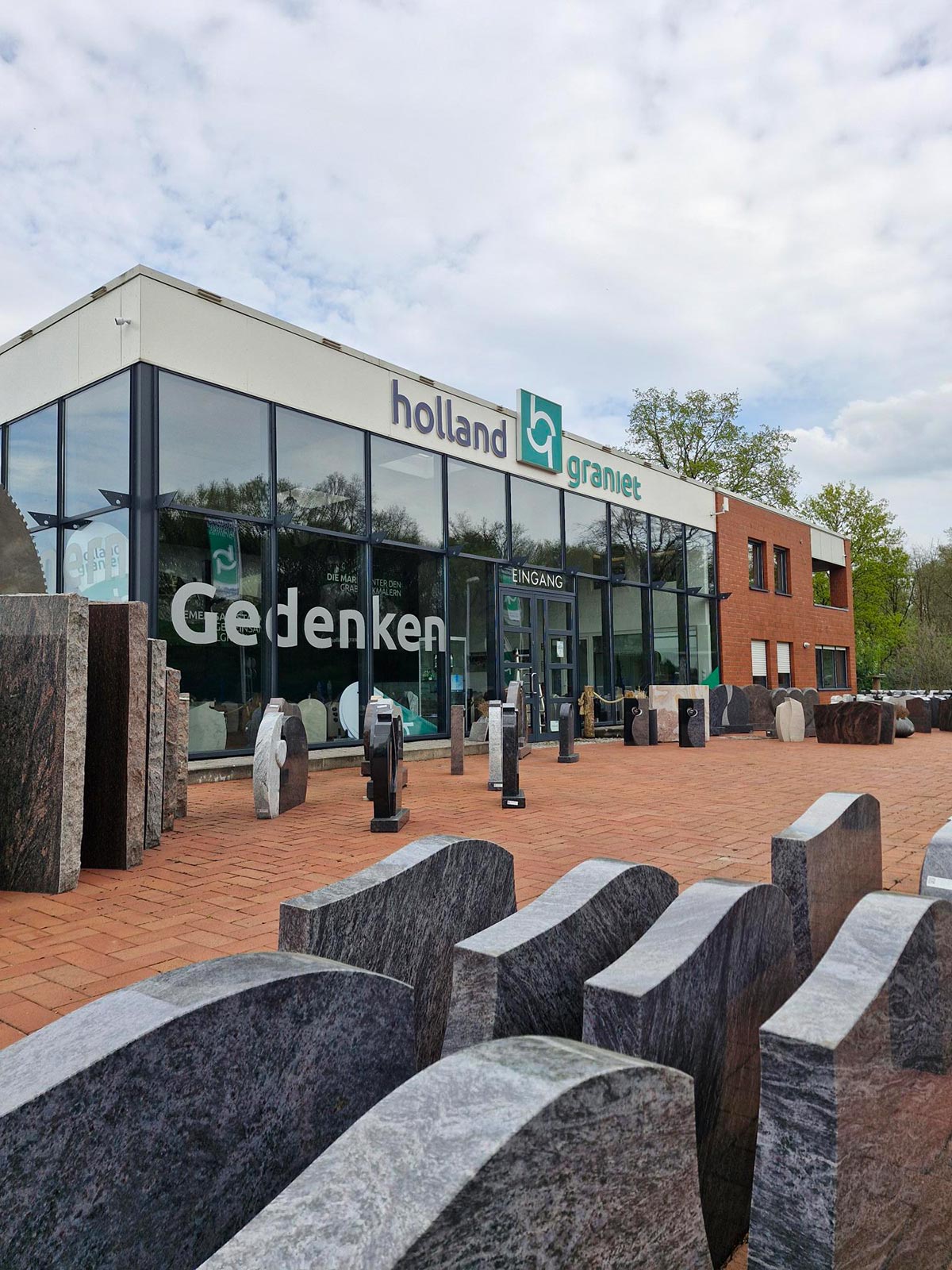 Modern Gebäude mit Glasfront, roten Backsteinen und dunklen Grabsteinen davor