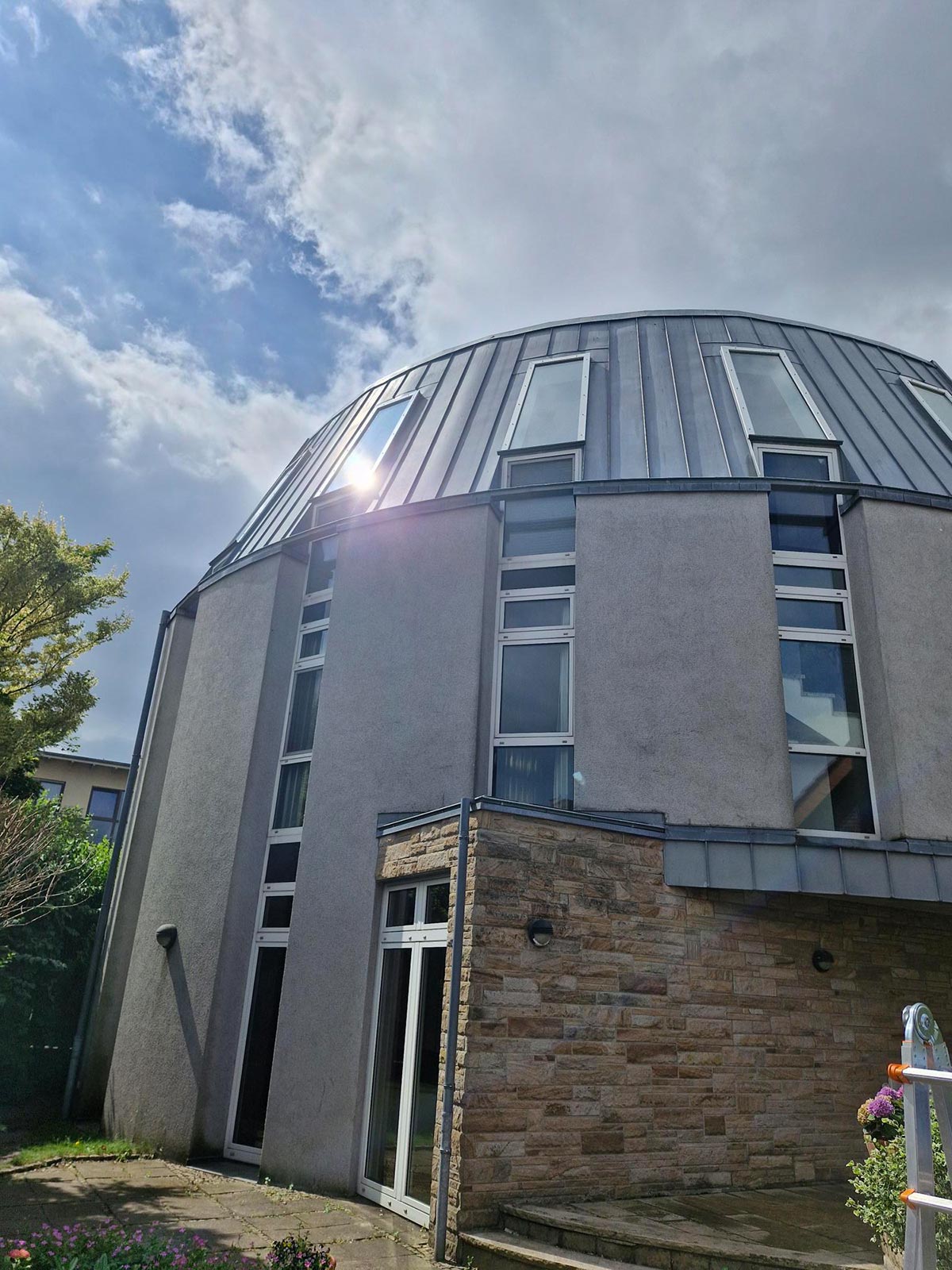 Ein modernes rundes Gebäude mit grauer Fassade, vielen Fenstern und Sonnenschein