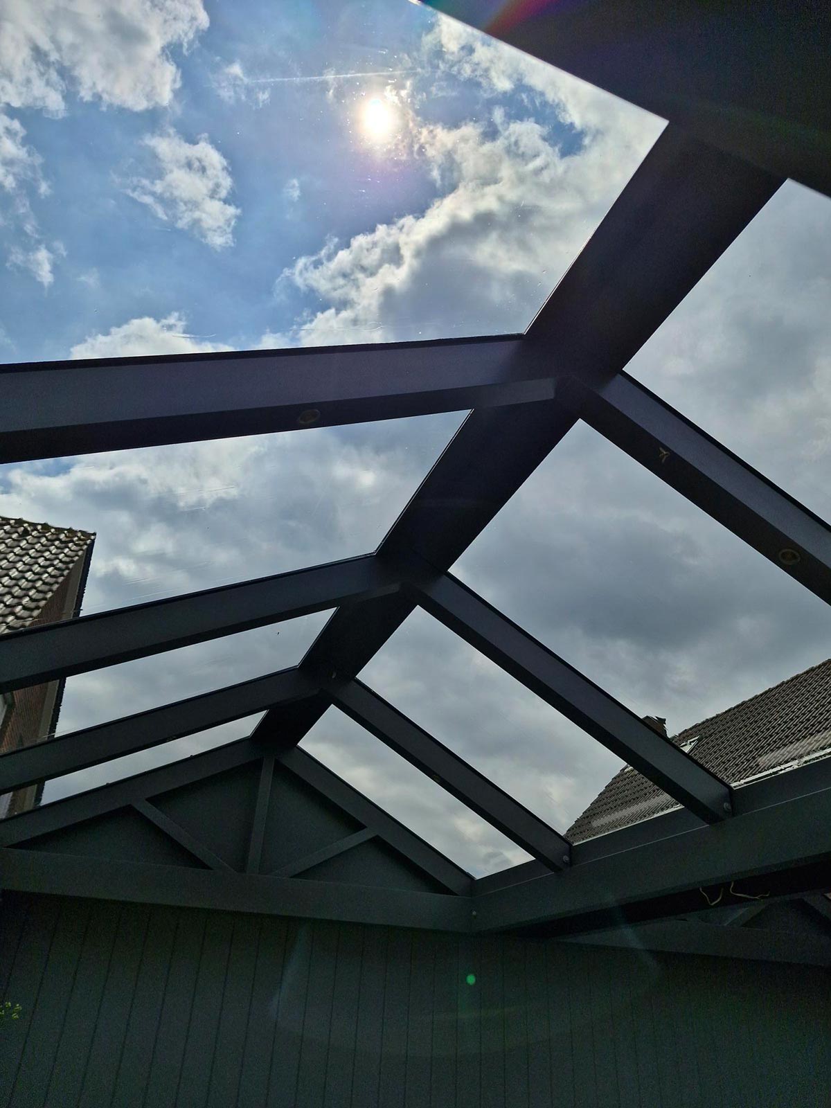Eine moderne schwarze Dachkonstruktion mit Sonnenlicht und teils bewölktem Himmel