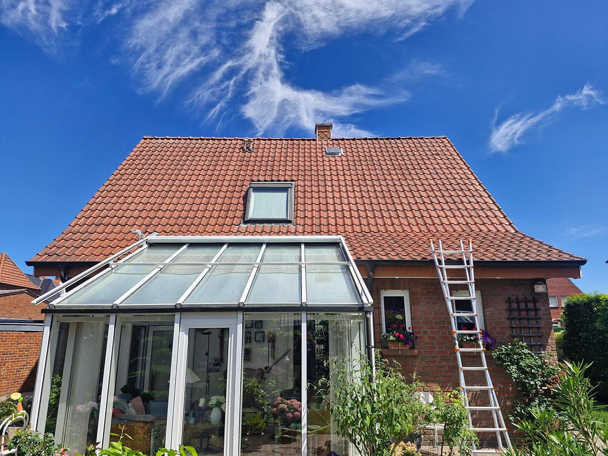 Ein Ziegelhaus mit Wintergarten, rotem Dach und Leiter an der Fassade unter blauem Himmel