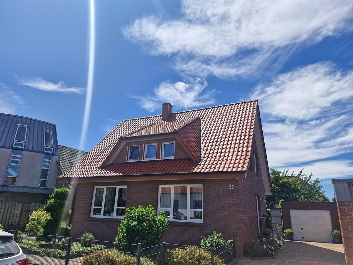 Ein Backsteinhaus mit rotem Ziegeldach steht im Sonnenschein unter blauem Himmel