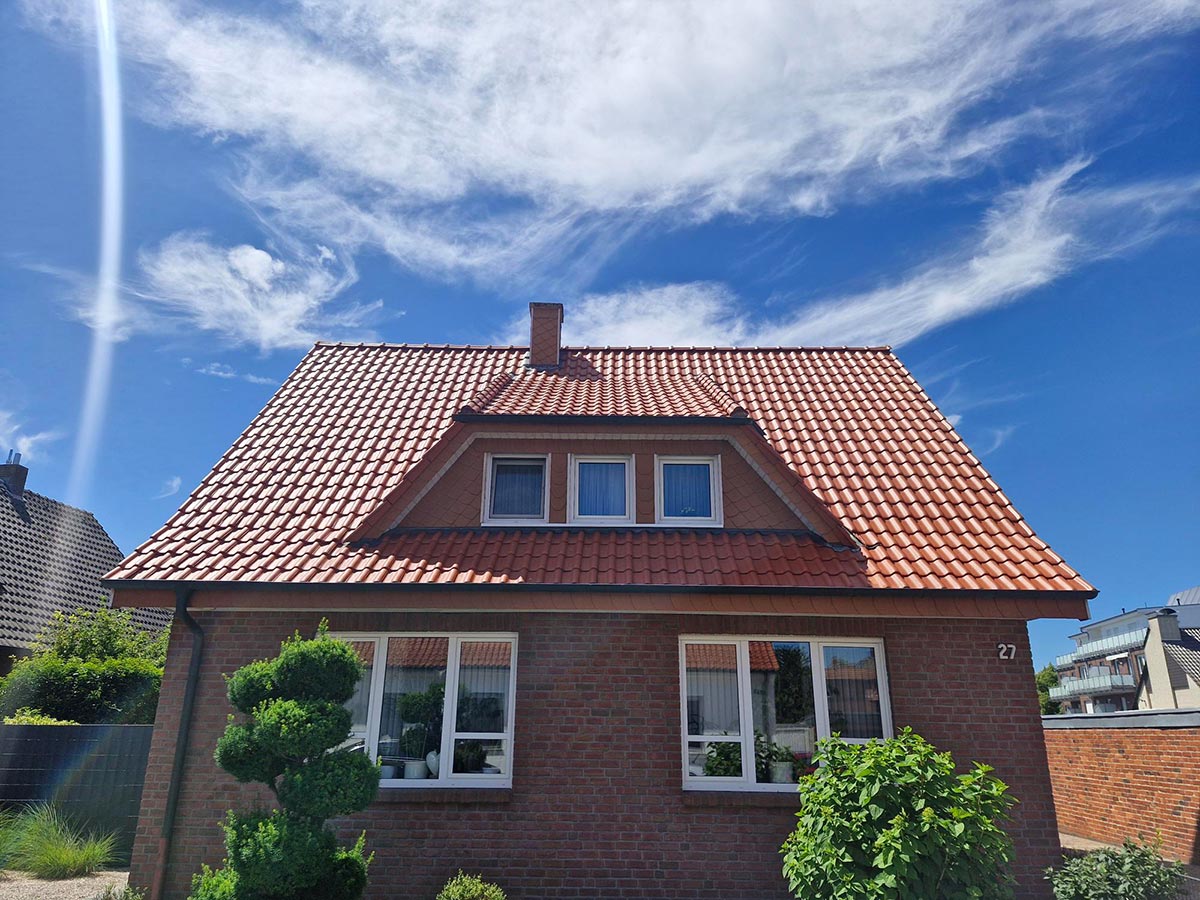 Backsteinhaus mit rotem Dach und weißen Fenstern unter blauem Himmel mit Wolkenformation