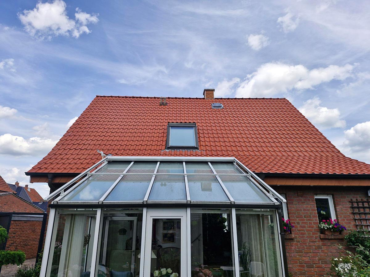 Ein rotes Ziegeldachhaus mit Wintergarten und blühenden Blumen am Fenster