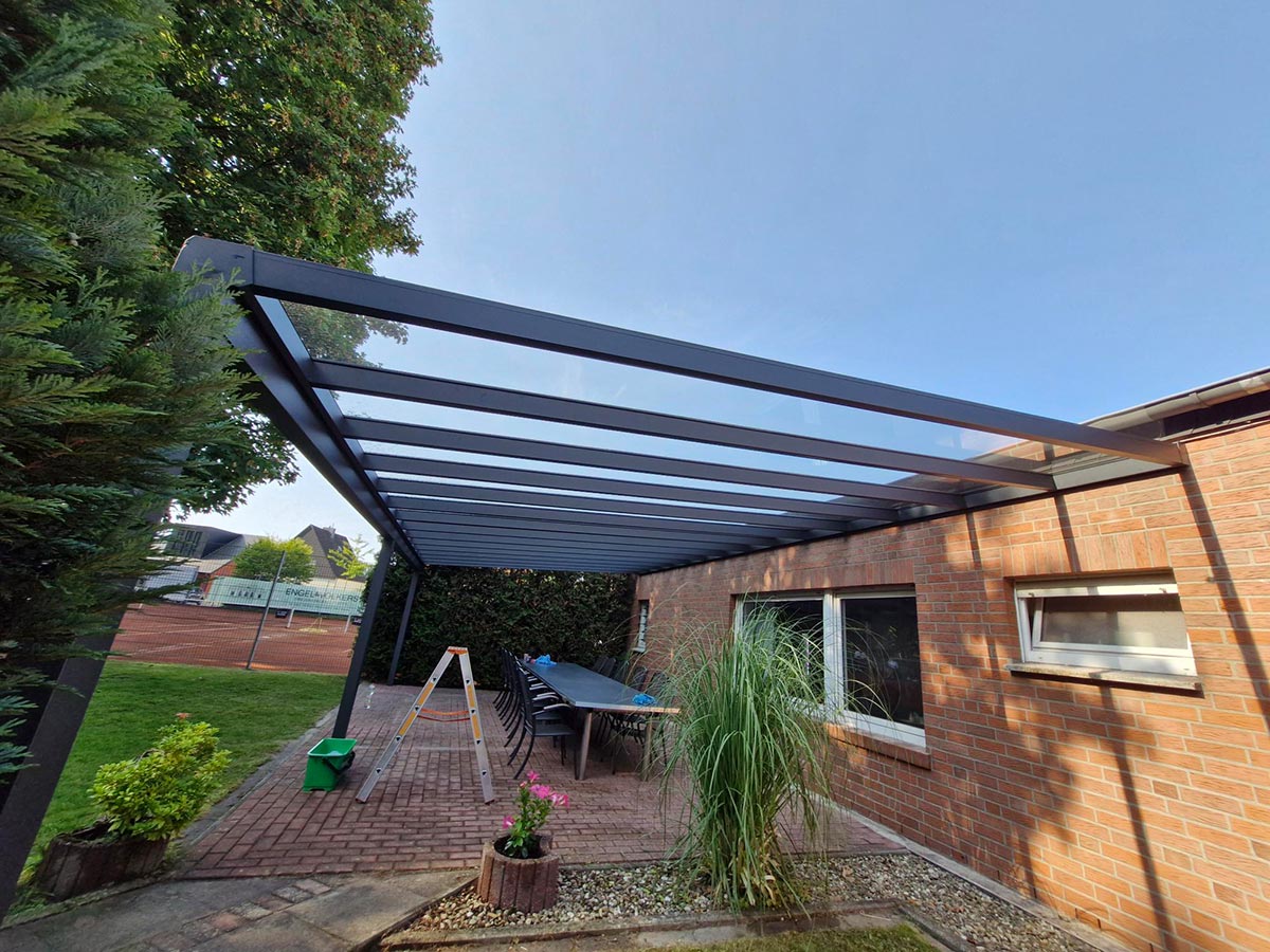 Eine überdachte Terrasse mit Glasdach neben einem Backsteinhaus und Sitzgruppe