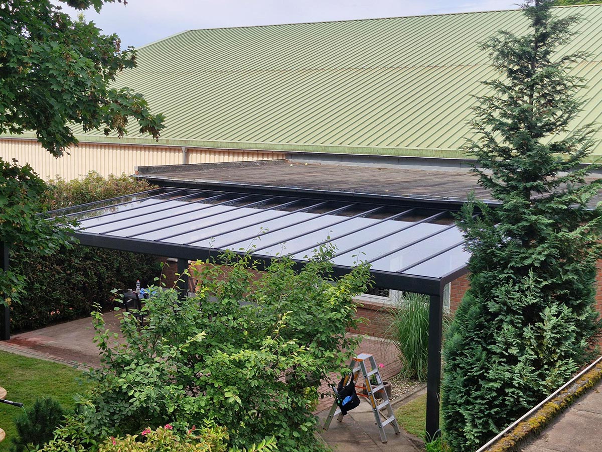 Eine Person mit dunklen Haaren sitzt entspannt unter einer modernen Glasüberdachung im Garten