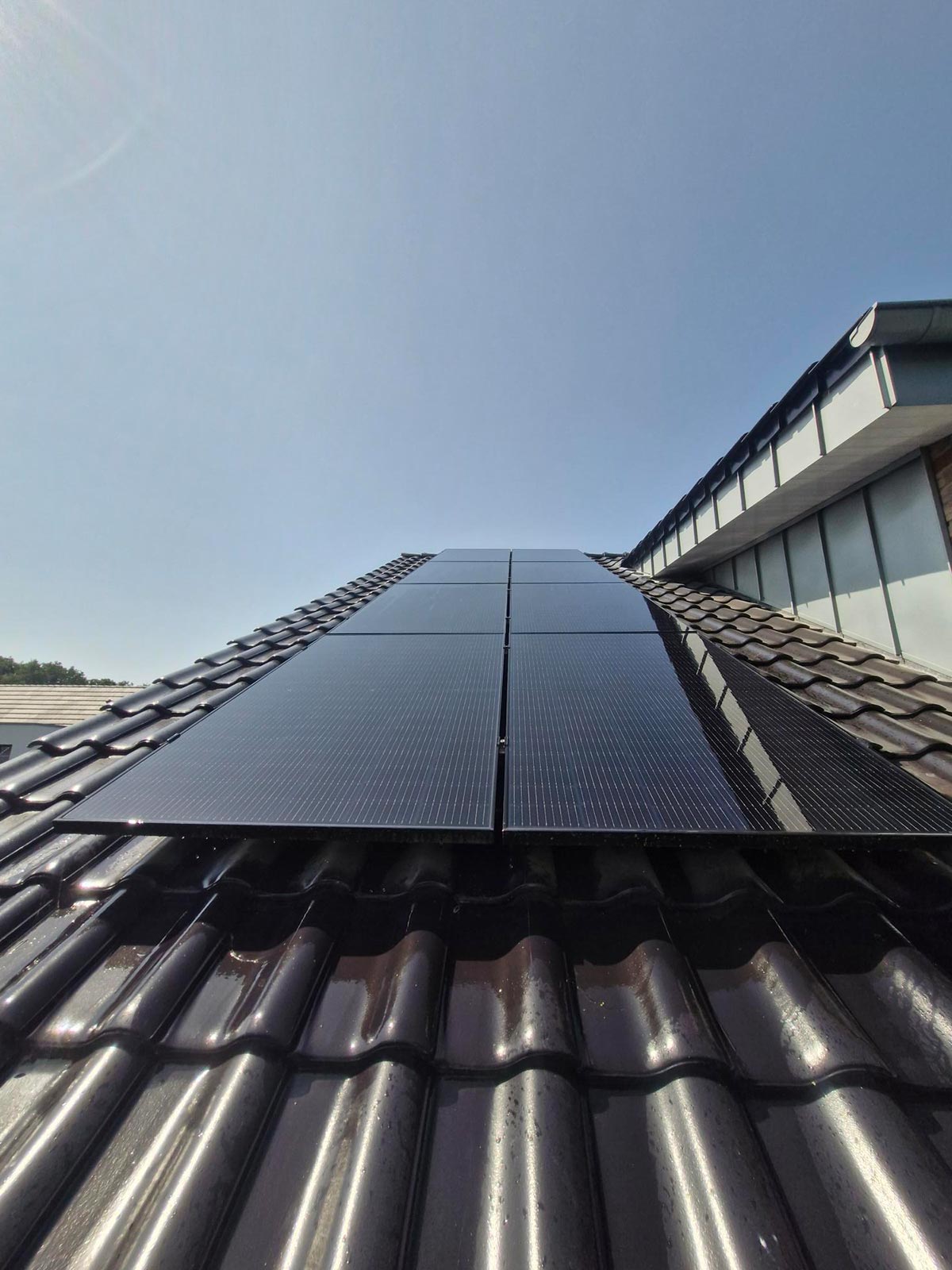 Eine Reihe schwarzer Solarpanels auf einem glänzenden Ziegeldach bei Sonnenschein